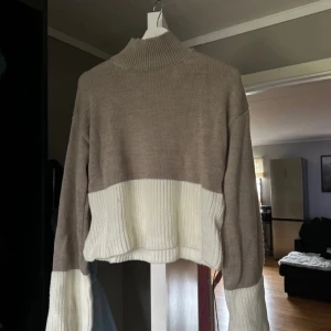 Beige och vit stickad tröja - Säljer en superfin stickad tröja i beige och vitt. Den har en hög krage och långa ärmar, perfekt för kyliga dagar. Tröjan är croppad och har en mysig, oversized passform. Perfekt för höst och vinter! 🧣✨Knappt använd.