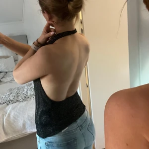 Svart glittrig halterneck topp - Snygg svart halterneck topp med guldglittriga detaljer. Toppen har en djup urringning och öppen rygg. Perfekt för en kväll ute eller festliga tillfällen✨✨ Inga defekter