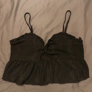 Svart topp - Snygg svart topp med smala axelband och volangdetaljer. Toppen har en smockad baksida för bättre passform och ett fint broderat mönster. Perfekt för en stilren look.