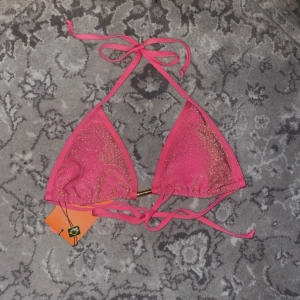 Rosa glittrig bikini - Snygg rosa bikini med glittriga detaljer. Överdelen har trekantsform och knytband i nacken och ryggen. Underdelen har knytband på sidorna för justerbar passform. Perfekt för en dag på stranden eller vid poolen.