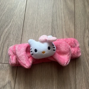 Rosa diadem med Hello Kitty - Sött rosa diadem med en mjuk Hello Kitty-figur i mitten. Perfekt för att ge en gullig touch till din look. Diademet är fluffigt och bekvämt att bära.