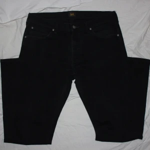 Svarta jeans från Lee - Snygga svarta jeans från Lee med klassisk femficksdesign. Perfekta för en stilren look. Passformen är straight och de är tillverkade i ett slitstarkt material.