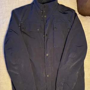 Field jacket Tommy Hilfiger - Snygg mörkblå jacka från Tommy Hilfiger med knappar och broderad logga på bröstet. Jackan har en stilren design med långa ärmar och praktiska fickor framtill. Perfekt för en stilren look.