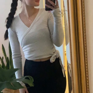 Vit omlottopp med knytband gymshark  - Säljer vit/cremefärgad omlottopp med långa ärmar och knytband i midjan från märket gymshark. Den är i bra skick :)