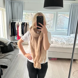 Beige halsduk från Zara - Säljer en supermjuk och fluffig beige halsduk från Zara. Perfekt för att hålla sig varm under kyliga dagar. Den har en stilren design som passar till det mesta. 27% ull och 8% alpacka ull. 