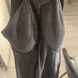 Glittrig svart långklänning - Snygg svart/blå långklänning med glittrigt mönster som ger en elegant touch. Perfekt för festliga tillfällen. Klänningen har en smickrande passform och är tillverkad i ett material som ger en fin lyster. Använt en gång 