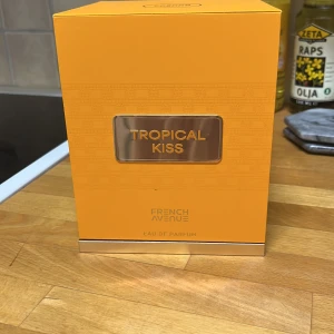 Tropical Kiss Eau de Parfum från French Avenue - Upptäck Tropical Kiss Eau de Parfum från French Avenue. Denna parfym kommer i en elegant orange flaska med guldiga detaljer och en matchande förpackning. Perfekt för den som älskar en tropisk doftupplevelse.
