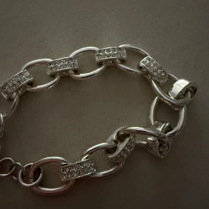 Silverarmband från Snö Of Sweden - Snyggt silverarmband från Snö Of Sweden med stora länkar dekorerade med glittrande stenar. Armbandet har en rund berlock med märkets logotyp. Perfekt till vardags som fest ❣️