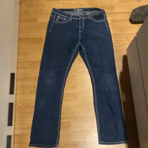 Mörkblå y2k jeans från Love Nation - Snygga mörkblå jeans från Love Nation med dekorativa bakfickor. Tillverkade i en bomullsblandning för extra komfort och stretch. Perfekta för en avslappnad stil med en touch av detaljer.