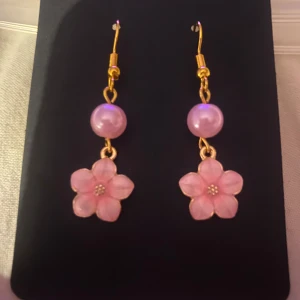 Rosa blommiga örhängen med pärlor - Egengjorda örhängen med rosa blommor och pärlor. De har en guldig krok och en hängande design som ger en söt och feminin touch. Perfekta för att lägga till en färgklick till din outfit.