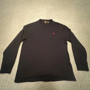 Svart långärmad tröja från Polo Ralph Lauren - Säljer en stilren svart långärmad tröja från Polo Ralph Lauren med det klassiska röda logotypen på bröstet. Tröjan har en rund halsringning och är tillverkad i mjukt material för en bekväm passform. Perfekt för en avslappnad look. Väldigt fint skick, skicka om eventuella funderingar.