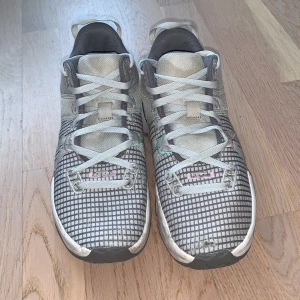 Nike Witness VII sneakers - Snygga Nike Witness VII sneakers med ett rutigt mönster i grått och vitt. Skorna har en unik design med turkosa detaljer och snörning. Perfekta för träning eller vardagsbruk.