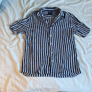 Randig skjorta från Only & Sons - Snygg kortärmad skjorta från Only & Sons med blå och vita ränder. Skjortan har knappar framtill och en klassisk krage. Perfekt för en avslappnad stil.