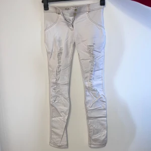 Vita byxor från Freddy - Snygga vita byxor från Freddy med tight passform och hög midja. Byxorna har dekorativa sömmar och en unik design med dragkedja fram. Perfekta för en stilren look.