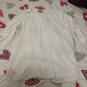 Vit blus från VERO MODA - Snygg blus i satin från H&M. Lös och bekväm passform med knappar vid ärmsluten, fint skick. Hör av dig vid intresse!😁
