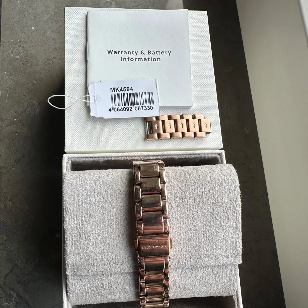 Snygg roséguldfärgad klocka från Michael Kors med glittriga detaljer runt urtavlan. Urtavlan har ett mönster med MK-loggan och är prydd med små stenar vid varje timme. Armbandet är i metall och justerbart med extra länkar. Perfekt för att ge en touch av lyx till din stil.. Asusteet.