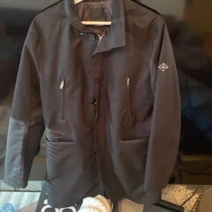 J.Lindeberg kappa - Säljer min J.lindeberg kappa då jag inte har användning av den, den är använd ett fåtal gånger och är i väldigt bra skick. En snygg svart kappa som fångar väldigt mycket komplimanger.                           —————————————————————Beskrivning:                                                                            Storlek 48, materialet är samma som en vanlig jacka, 