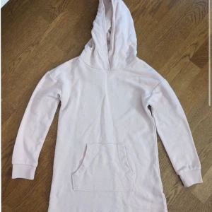 Lång vit hoodie med ficka - Säljer en mysig vit lång hoodie med en stor ficka framtill. Tröjan har långa ärmar och en rymlig huva, perfekt för kyliga dagar. Passar bra för en avslappnad stil.
