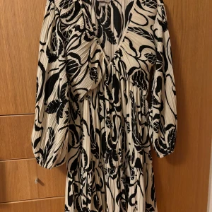 Svartvit mönstrad klänning - Klänning från H&M med ett abstrakt/blommigt mönster. Svart och offwhite. Helt slutsåld. Nyskick endast använd vid två tillfällen. Passar både storlek M och S då den är stretchig. Luftig och lätt så den funkar på sommarn!