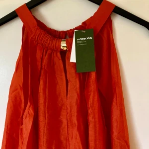 Orange klänning från H&M Conscious - Snygg orange klänning från H&M Conscious med en luftig passform. Klänningen har breda axelband och en enkel design som passar perfekt för varma dagar. Tillverkad i ett lätt och bekvämt material.