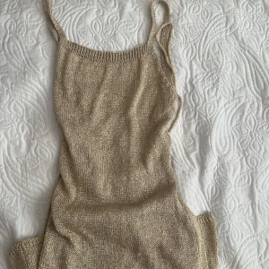 Beige stickad klänning - Snygg beige stickad klänning med smala axelband och trendig snörning i ryggen. Perfekt för en stilren look. Aldrig använd, köptes i Marbella
