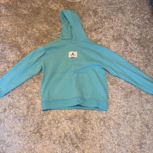 Turkos hoodie från Jordan - Säljer en snygg turkos hoodie från Jordan med det ikoniska Jumpman-logotypen på bröstet. Hoodien har en stor ficka framtill och justerbar huva med dragsko. Perfekt för en avslappnad stil.