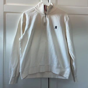 Vit tröja med dragkedja från Tommy Hilfiger - Säljer en stilren vit tröja från Tommy Hilfiger med halv zip och broderad logga på bröstet. Tröjan har långa ärmar och en klassisk design. Storleken är i XL men passformen är M då jag jag L och den är för liten. Nypris runt 1000 kr. 