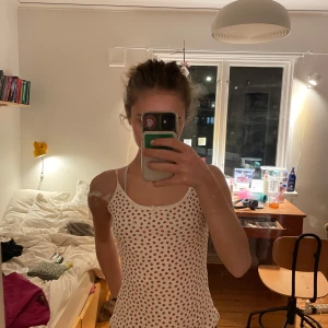 Vit linne med röda prickar från Brandy Melville - Säljer ett sött vitt linne från Brandy Melville med små jordgubbsmönster. Linnet har smala axelband och en liten rosett. Har sytt up axelbanden då den var förstår för mig men dem kan lätt sprättas upp💗 Skulle säga att linnet passar både Xs och S💗🙌 Linnet har en lite fläck men skulle tro att den tas bort enkelt