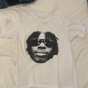 Vit t-shirt med tryck från 2crazy - Säljer en vit t-shirt från 2crazy med ett stort svartvitt tryck av ett ansikte med solglasögon på framsidan. T-shirten har en klassisk rund hals och korta ärmar. Perfekt för en cool och avslappnad stil.