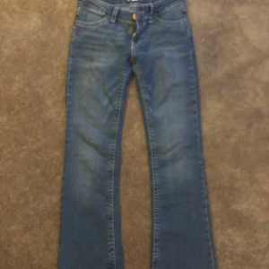 Blå bootcut jeans - Snygga blå bootcut jeans med klassisk femficksdesign och kontrastsömmar. De har en knapp och dragkedja framtill samt dekorativa knappar på bakfickorna. Perfekta för en avslappnad stil.