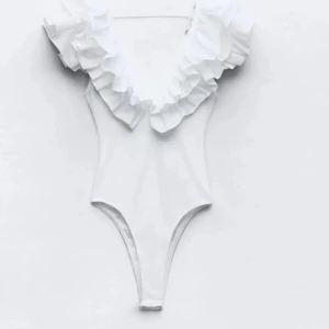 Vit body med volangdetaljer - Snygg vit body med djup v-ringning och volangdetaljer runt halsen från Zara. Använd 2 ggr men inte riktigt min stil! 