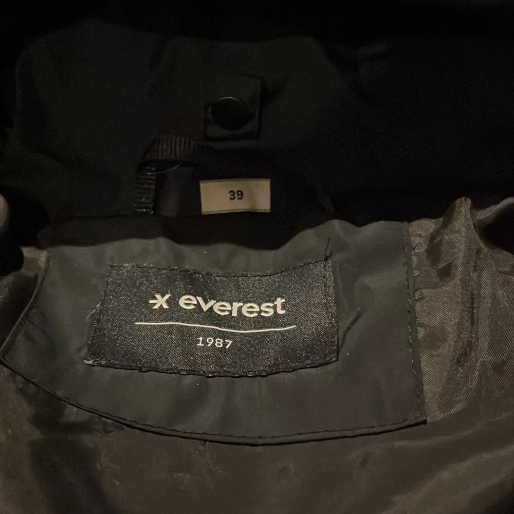 Säljer en lång svart dunkändla jacka från Everest med huva och dragkedja. Reflexslitsar Jackan har långa ärmar och praktiska fickor framtill. Perfekt för kyliga dagar.. Takit.