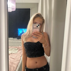 Svart glittrig tubtopp från SHEIN - Snygg svart tubtopp från SHEIN, täckt med glittrande paljetter. Perfekt för en kväll ute eller festliga tillfällen. Toppen är croppad och ger en trendig look. aldrig använd och storlek S