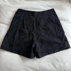 Svarta shorts med broderad design - Snygga svarta shorts med en unik broderad design som ger en stilren look. Perfekta för varma dagar när du vill ha något bekvämt men ändå trendigt. De har en normal passform och är tillverkade i ett lätt material som andas.