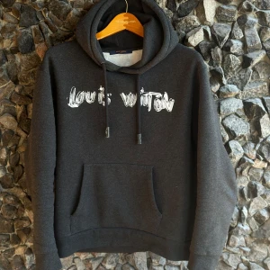 Svart hoodie från Louis Vuitton - Snygg svart hoodie från Louis Vuitton med tryckt logotyp på framsidan. Tröjan har en klassisk känguruficka och justerbar huva med dragsko. Perfekt för en stilren och bekväm look. Skriv vid frågor