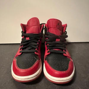 Nike Air Jordans i rött och svart - Snygga Nike Air Jordans i en klassisk röd och svart färgkombination. Skorna har en hög design med svart snörning och den ikoniska Nike-loggan på sidan. Perfekta för dig som vill ha en stilren och sportig look.