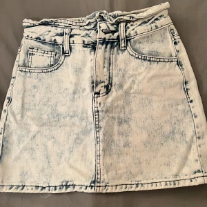  jeanskjol - Snygg acid wash jeanskjol med hög midja och dragkedja fram. Kjolen har klassiska femficksdetaljer och en kort längd som ger en cool look. Perfekt för en avslappnad stil.