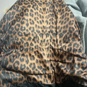 Leopardmönstrad jacka från Hollies - Snygg leopardmönstrad jacka från Hollies med svart utsida och leopardfoder. Jackan har dragkedja och flera praktiska fickor med dragkedjor. Perfekt för att hålla stilen i kallare väder.