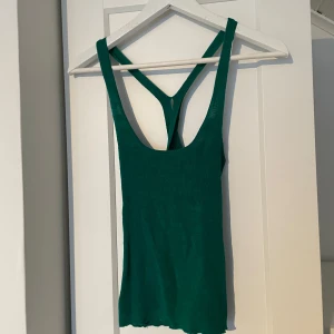 Grön ribbad linnetopp - Snygg grön ribbad linnetopp med smala axelband och korsad ryggdesign. Perfekt för varma dagar eller som lager under en jacka. Den stretchiga passformen gör den bekväm och stilren. Storlek S/M