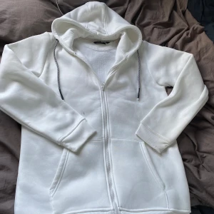 Vit zip hoodie från brave soul London - Säljer en stilren vit hoodie med dragkedja och justerbar huva. Perfekt för en avslappnad look. Den har långa ärmar och praktiska fickor framtill. Passar bra till både jeans och mjukisbyxor. Jag fick denna i födelsedagspresent och den har blivit använd möjligtvis 1 gång den är extremt bekväm och varm! Dm för frågor!!✨🔥