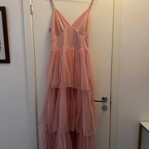 Rosa långklänning från Vila - Säljer en rosa långklänning från Vila. Har använt den en gång på min bal och säljer nu vidare den. Den har tunna axelband och volangdetaljer. Klänningen har ett prickigt mönster och en v-ringad design framtill. Perfekt för balen eller en annan festlighet!🌸