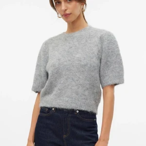 Grå stickad T-shirt  - Säljer en stilren och mjuk grå tröja från Vero moda med korta ärmar, vilket gör den perfekt för lager-på-lager. Den har en klassisk rund hals och en bekväm passform. Perfekt för både vardag och mer uppklädda tillfällen. Storleken på lappen är xl men jag skulle säga att den snarare motsvarar storlek m. Jag har själv storlek S och den är perfekt för en lite oversize look.
