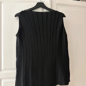 Svart ärmlös topp från Zara - Säljer en elegant svart ärmlös topp från Zara med plisserad design. Perfekt för en stilren look. Toppen har en rund halsringning och är tillverkad i ett lätt material.