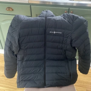 Svart dunjacka från Sail Racing - Säljer nu min defekt fri svart dunjacka från Sail Racing med dragkedja och huva. Jackan har jag haft i ägo i tre dagar använt den en gång den ser helt ny ut inga skador eller defekter på den. Pris kan diskuteras om du kontaktar mig men eftersom den är ny så går jag inte ner i pris mycket