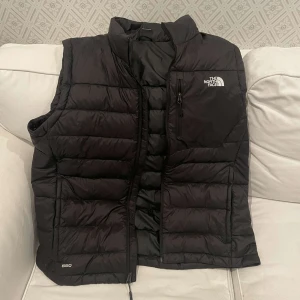 The North Face Väst - Svart dunväst från The North Face med vit loga. Helt oanvänd. Storlek XL. Ny 1500kr
