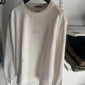 Vit sweatshirt från C.P. Company - Säljer en stilren sweatshirt från C.P. Company köpt från Harrods i London. Tröjan har en rund halsringning och en diskret logotyp på bröstet. Perfekt för en avslappnad look. Storlek S. Fåtal gånger använd. Bara att höra av sig vid frågor.