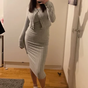 Grå ribbad klänning - Säljer en helt ny stilren grå klänning med en kofta till. Klänningen har en tight passform och är perfekt för kyligare dagar. Den är både bekväm och trendig, idealisk för en chic look.