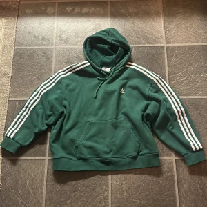 Grön hoodie från Adidas - Säljer en grön hoodie från Adidas med klassiska vita ränder längs ärmarna. Använda 2-3 gånger och är köpt i affär.