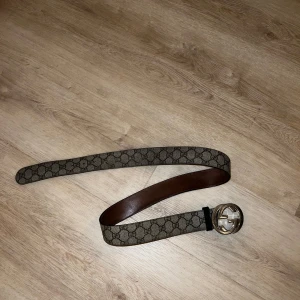 Gucci bälte med GG-mönster - Säljer ett stilrent Gucci bälte med det klassiska GG-mönstret. Bältet har en elegant brun insida och en iögonfallande silverspänne med GG-logotypen. Perfekt för att ge din outfit en lyxig touch. Strl 95