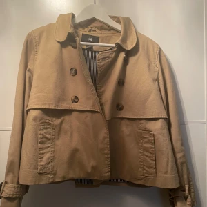 Beige kort trenchcoat  - Liten i storlek. Skulle passa en L, till och med kanske M. Använd fåtal gånger (2-3 ggr).